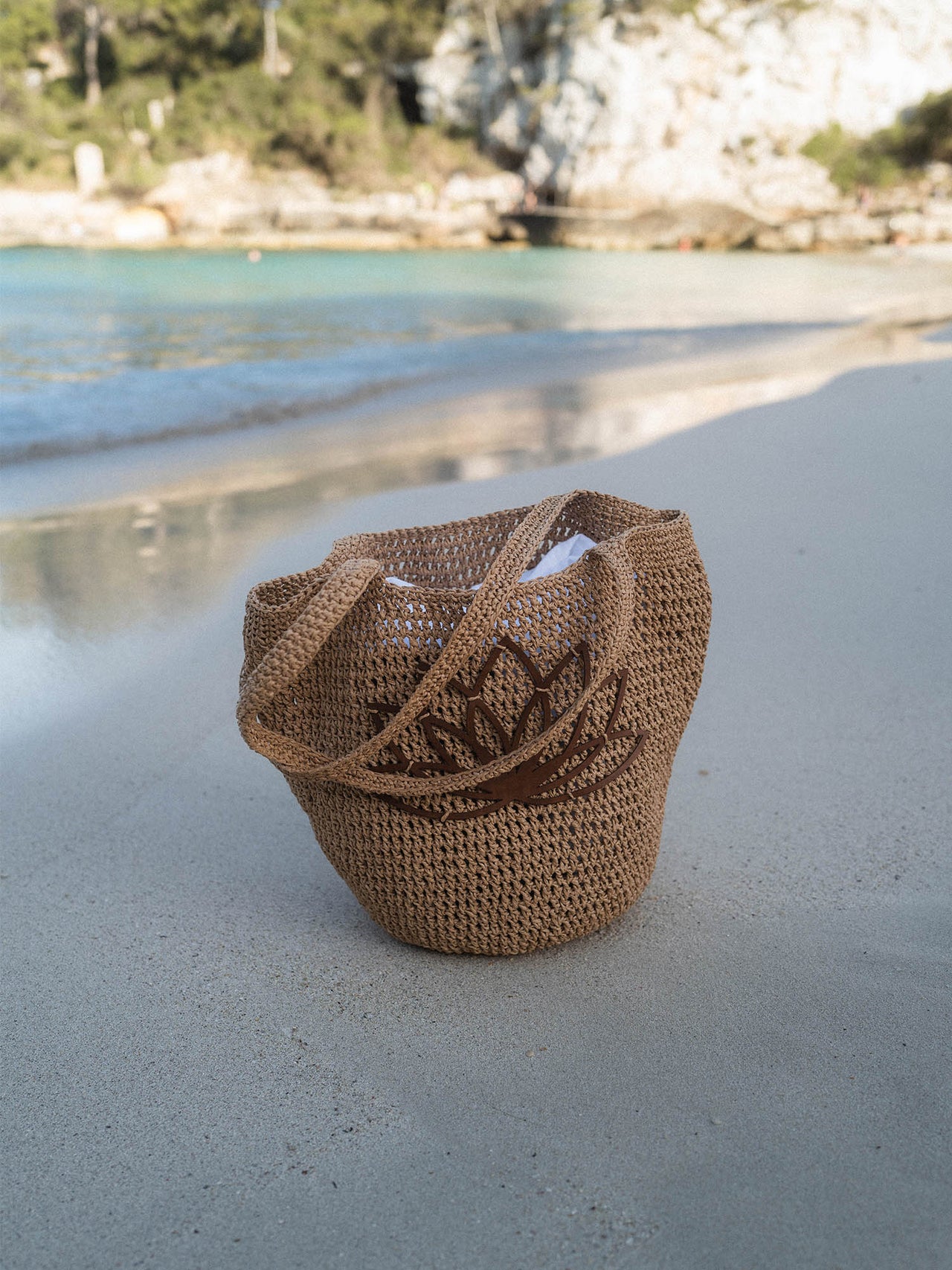Lotus Bucket Tasche aus cognacbraunem Bast mit PURELEI Lotusblume am Strand für sommerliche Leichtigkeit