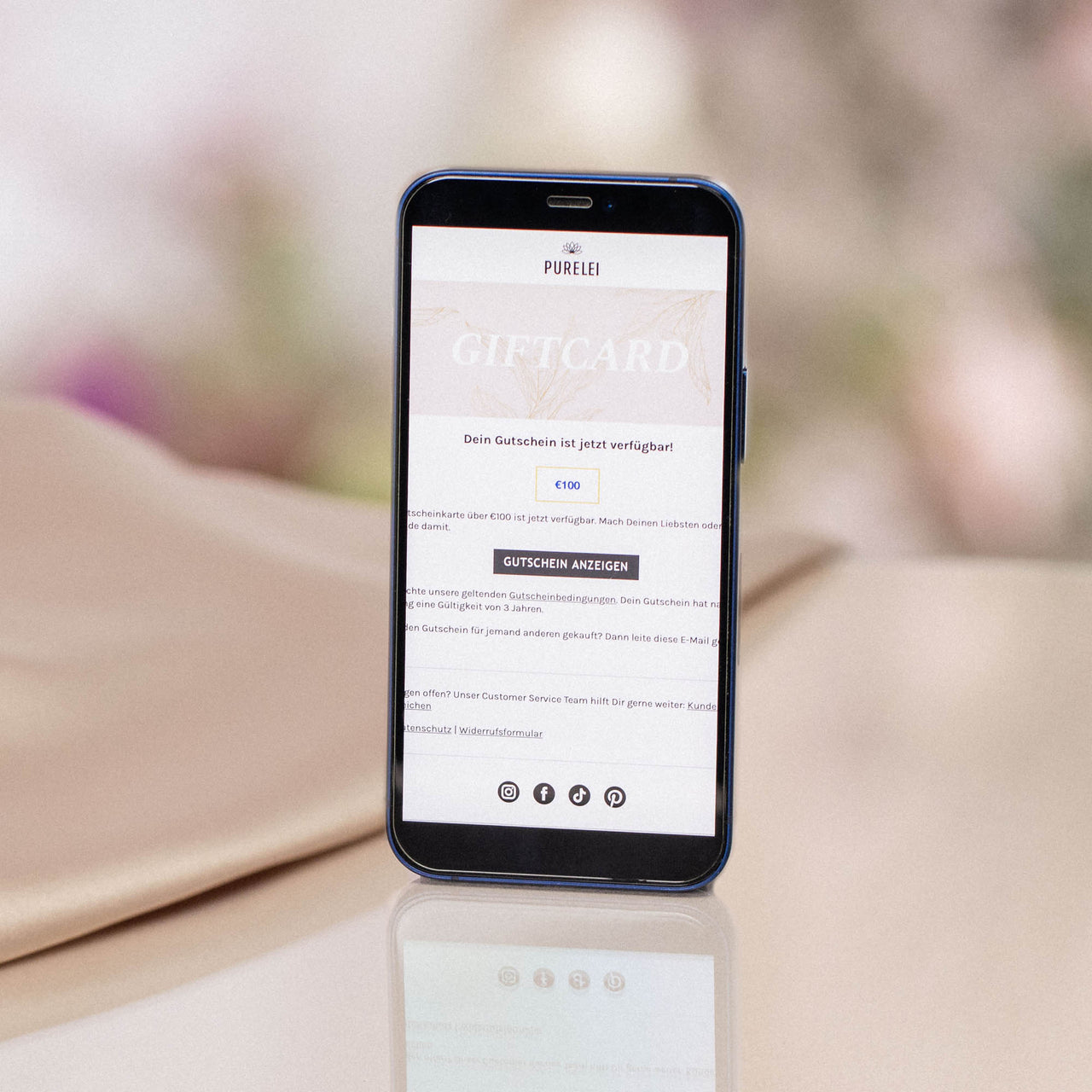 Smartphone zeigt PURELEI Gutschein per E-Mail 30€ auf hellem, sanft glänzendem Untergrund in eleganter Atmosphäre