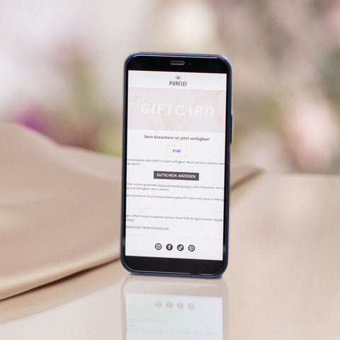 Smartphone zeigt PURELEI Gutschein per E-Mail 30€ auf hellem, sanft glänzendem Untergrund in eleganter Atmosphäre