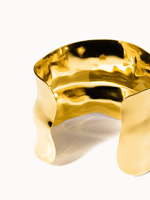 Goldenes, geschwungenes Armband von PURELEI mit glänzender Oberfläche und elegantem Design.