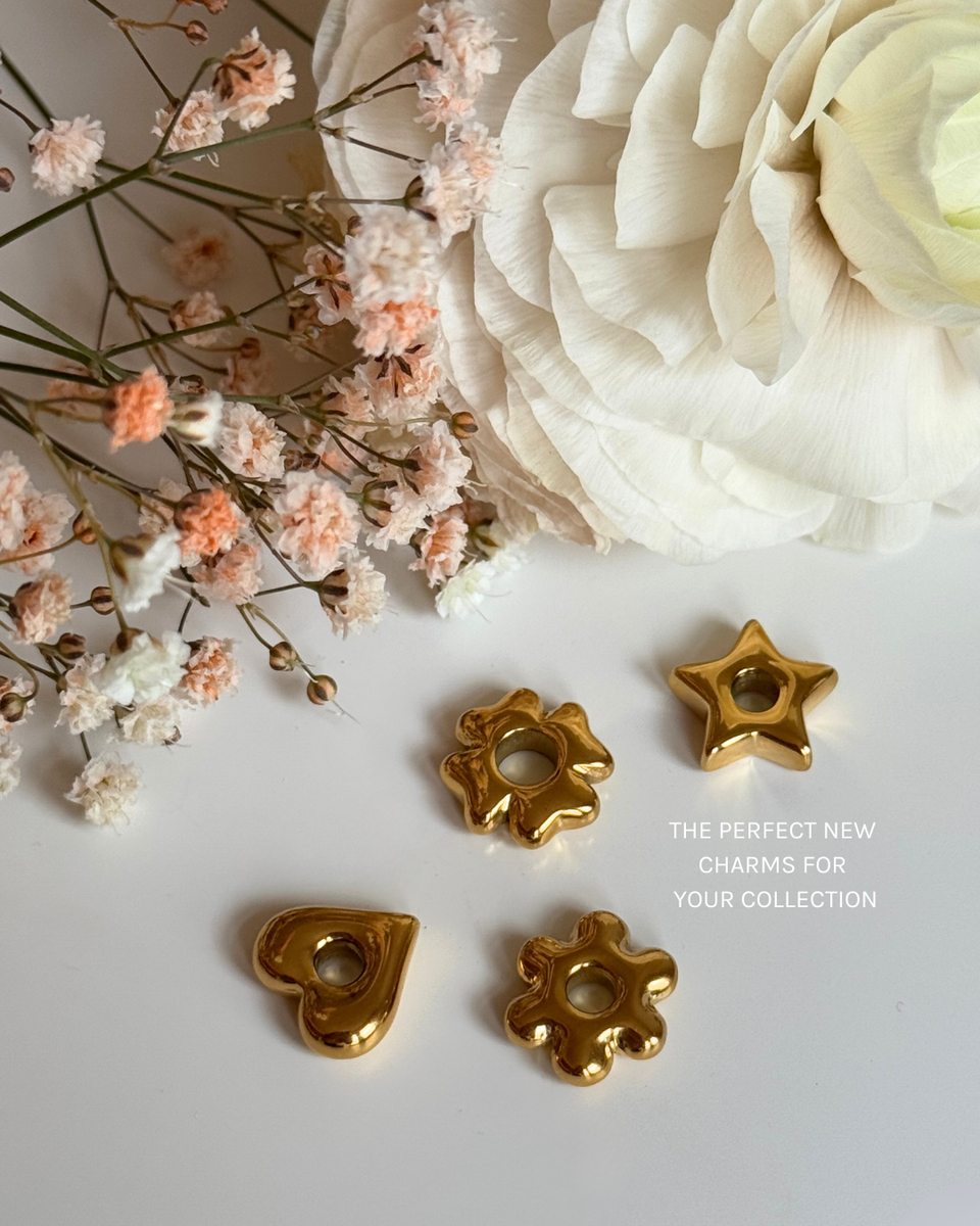 Goldener Flower Lucky Charm aus Edelstahl, fein poliert auf hellem Hintergrund mit zarten Blumen von PURELEI