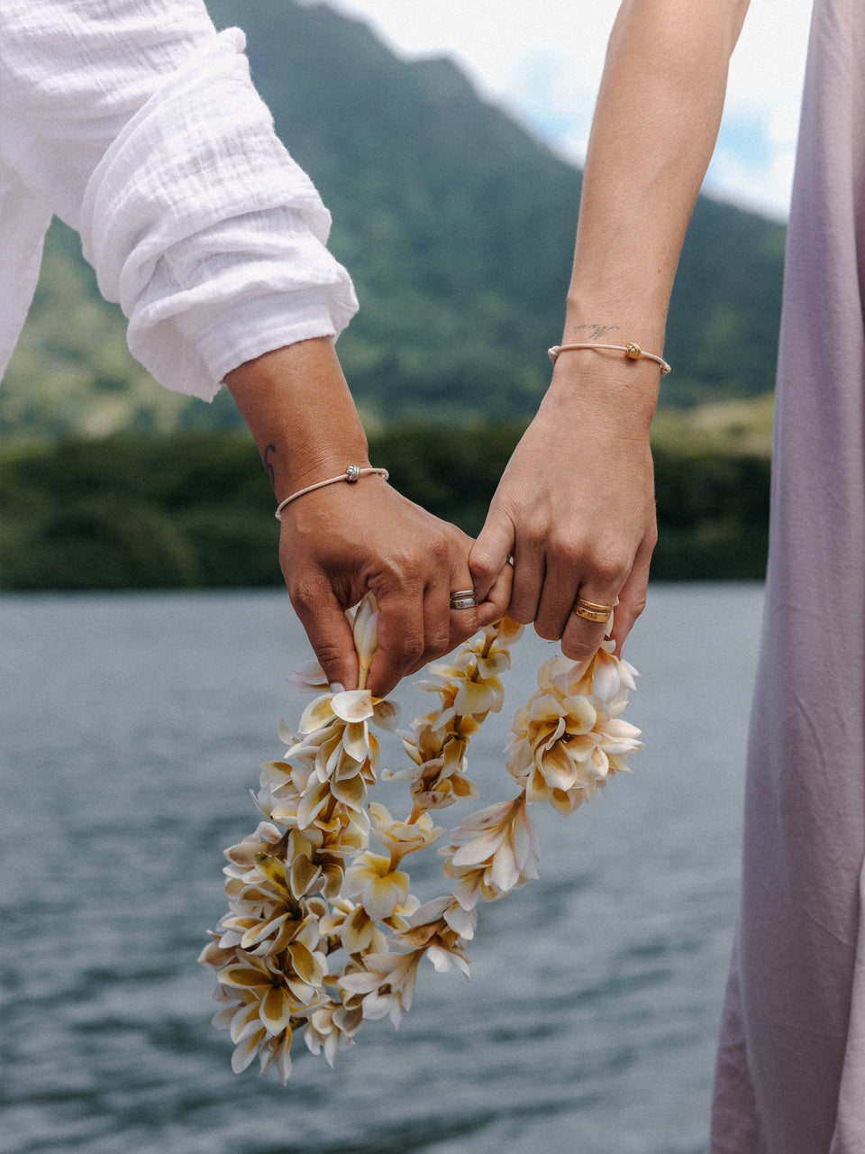 PURELEI Twin Tides Ring in Gold und Silber, elegant kombiniert am Finger mit tropischem Blumenschmuck am Seeufer