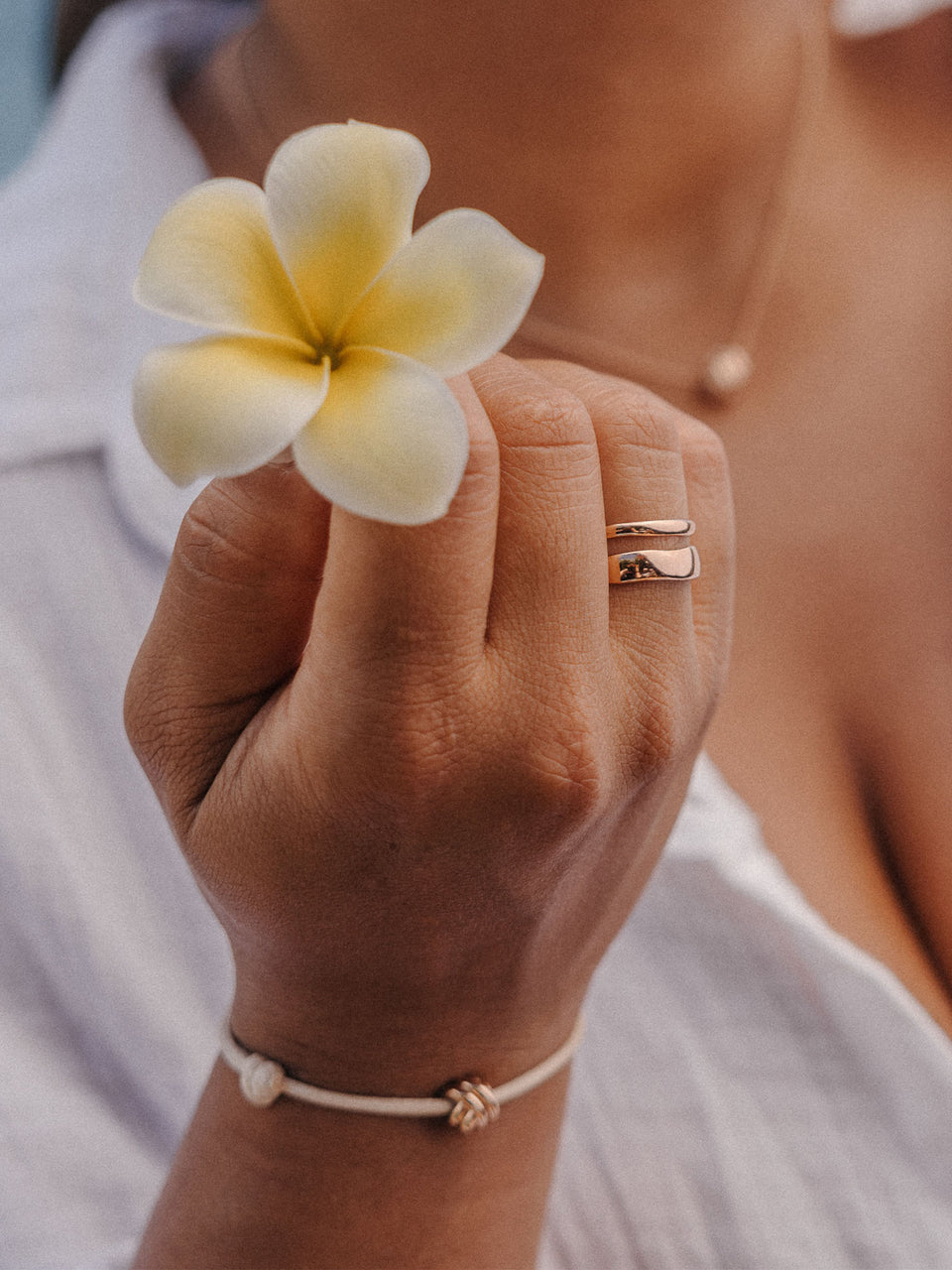 PURELEI Twin Tides Ring in 18K Gold, zwei geschwungene Bänder, getragen mit tropischer Blüte, warm und elegant.