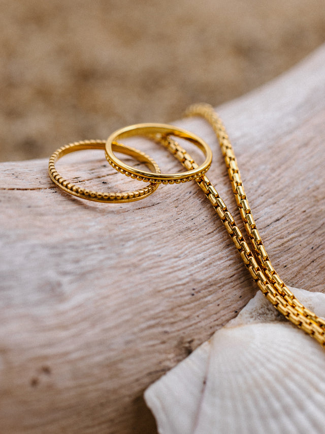 Drei goldene Ringe und eine Kette auf Holz, inspiriert von PURELEI.