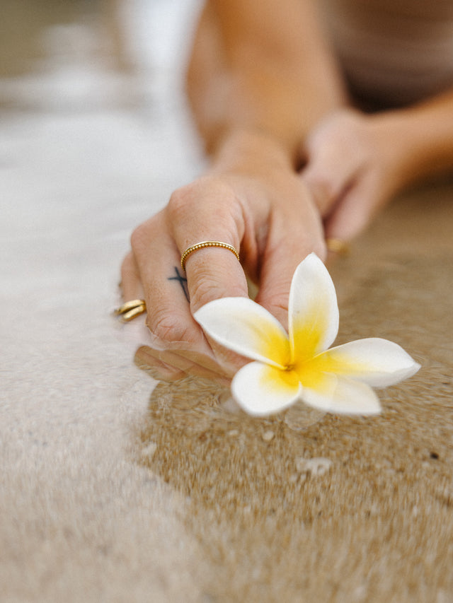 Händedetail mit goldenen Ringen und einer weißen Blüte im Wasser, PURELEI inspiriert.