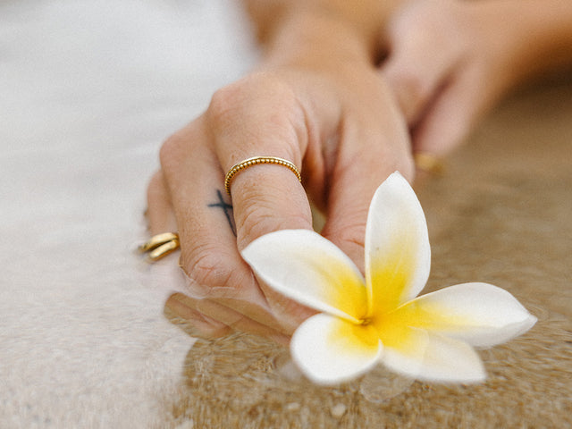 Goldring und Plumeria-Blüte, inspiriert von PURELEI, am Wasser reflektiert.