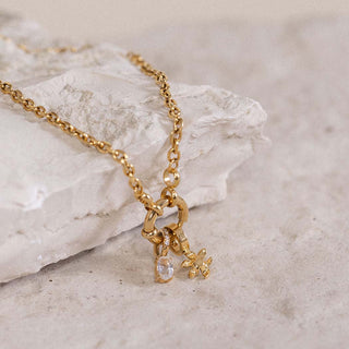 Goldene Kette mit funkelndem Anhänger auf hellem Stein, PURELEI inspiriert.