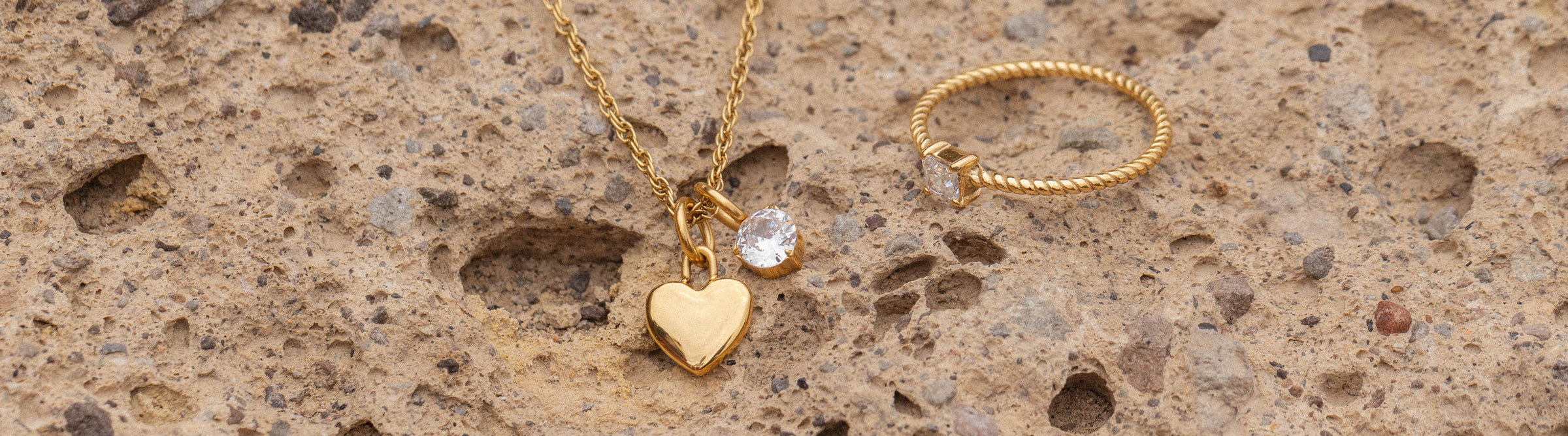 Goldene Herz-Kette und Ring auf hellem Lavagestein, PURELEI inspiriert.