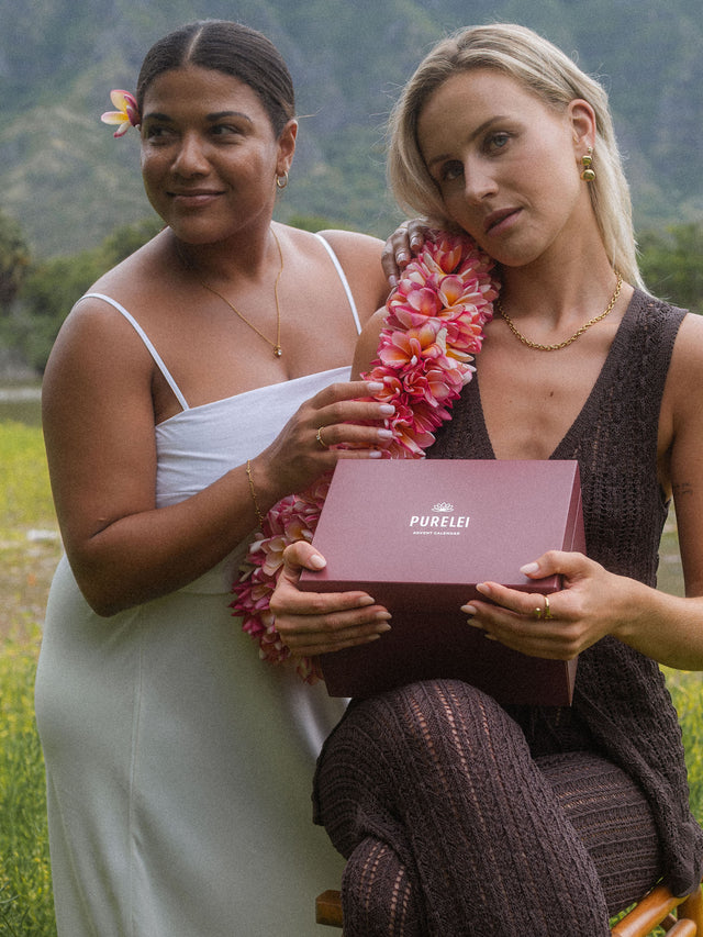 Zwei Frauen in eleganter Kleidung mit PURELEI-Box, umgeben von blühender Natur.