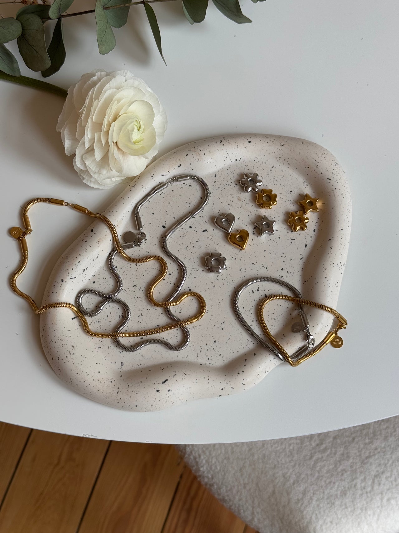 Flower Lucky Charm aus gold- und silberfarbenem Edelstahl, zarte Blütenanhänger auf weißer Keramik, PURELEI-Style.
