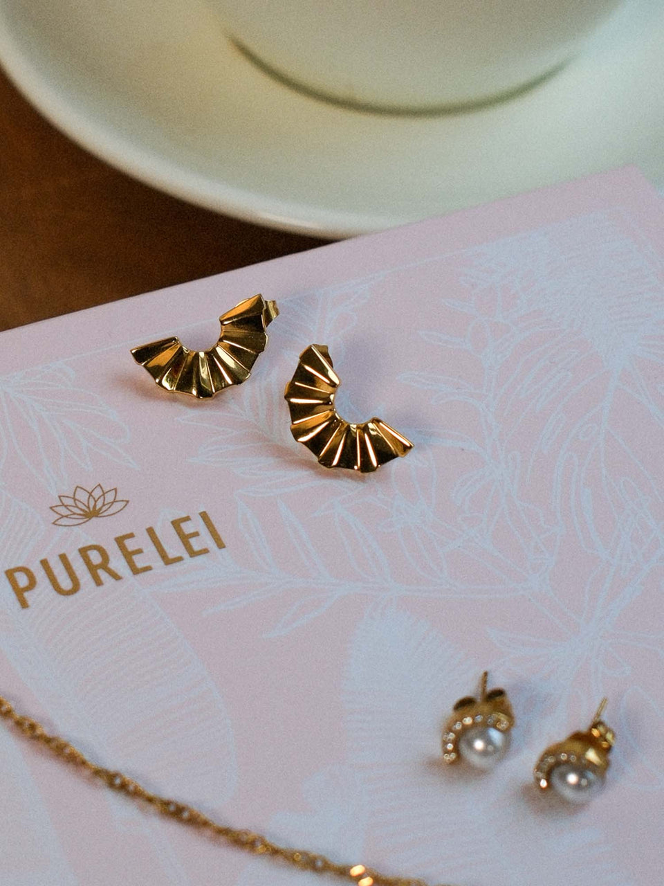 PURELEI Air Schmuckset mit vergoldeten Fan-Ohrringen auf zartem rosafarbenem Hintergrund inszeniert