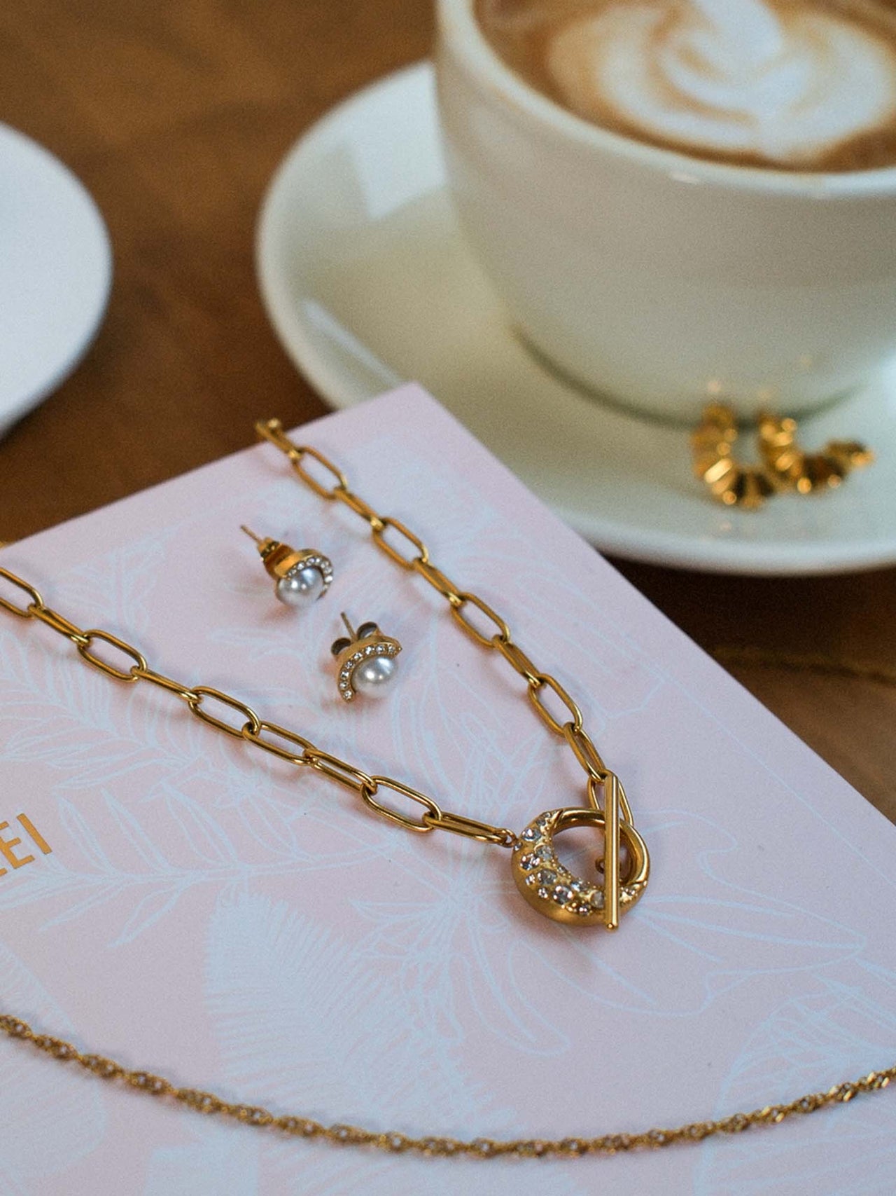 PURELEI Air Schmuckset mit goldener Gliederkette und Perlen-Ohrringen, elegant inszeniert mit Kaffee.