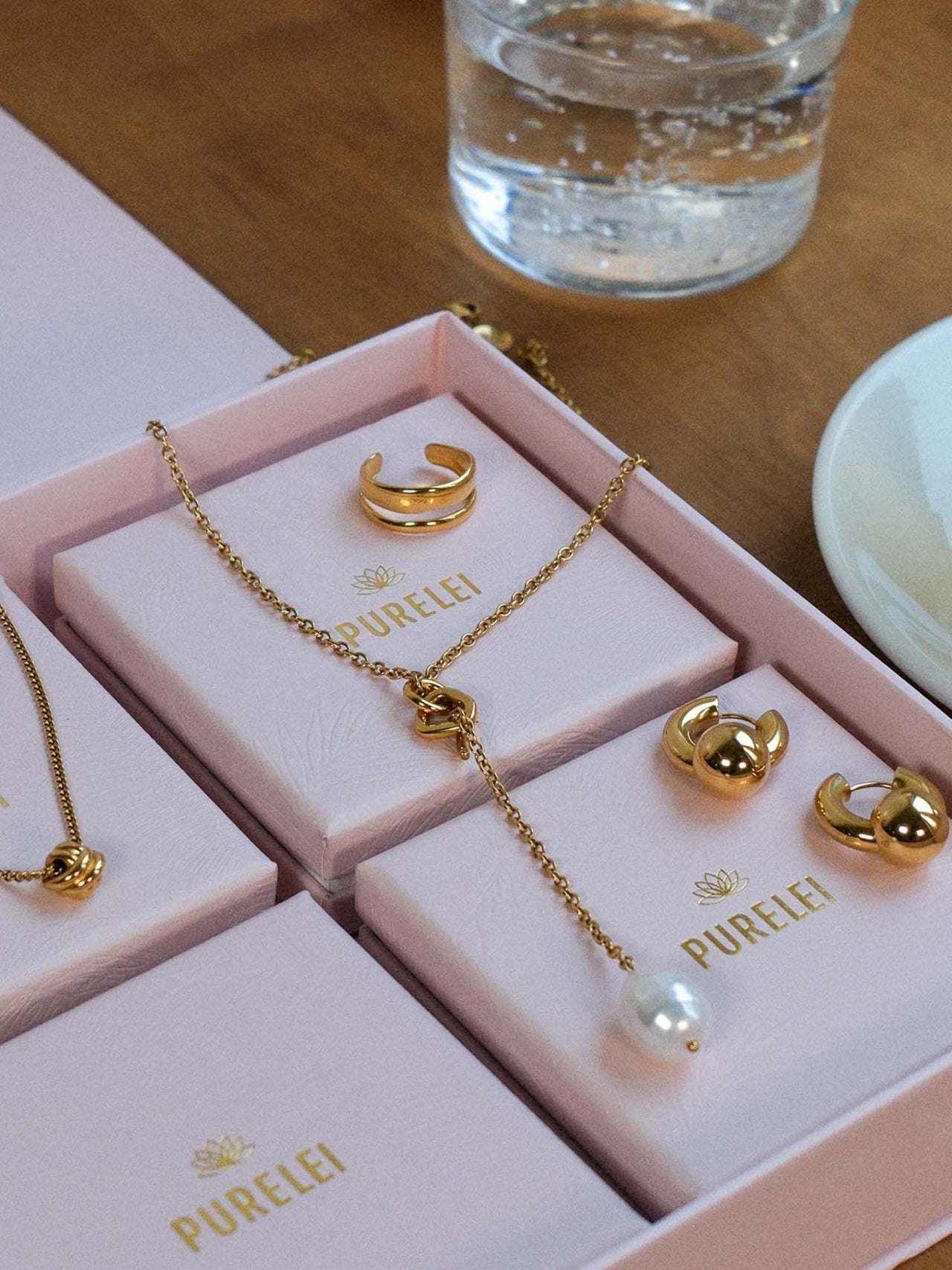 Aloha Schmuckset von PURELEI mit vergoldeter Knot-Kette, Perlen-Anhänger, Creolen und verstellbarem Ring, elegant inszeniert.