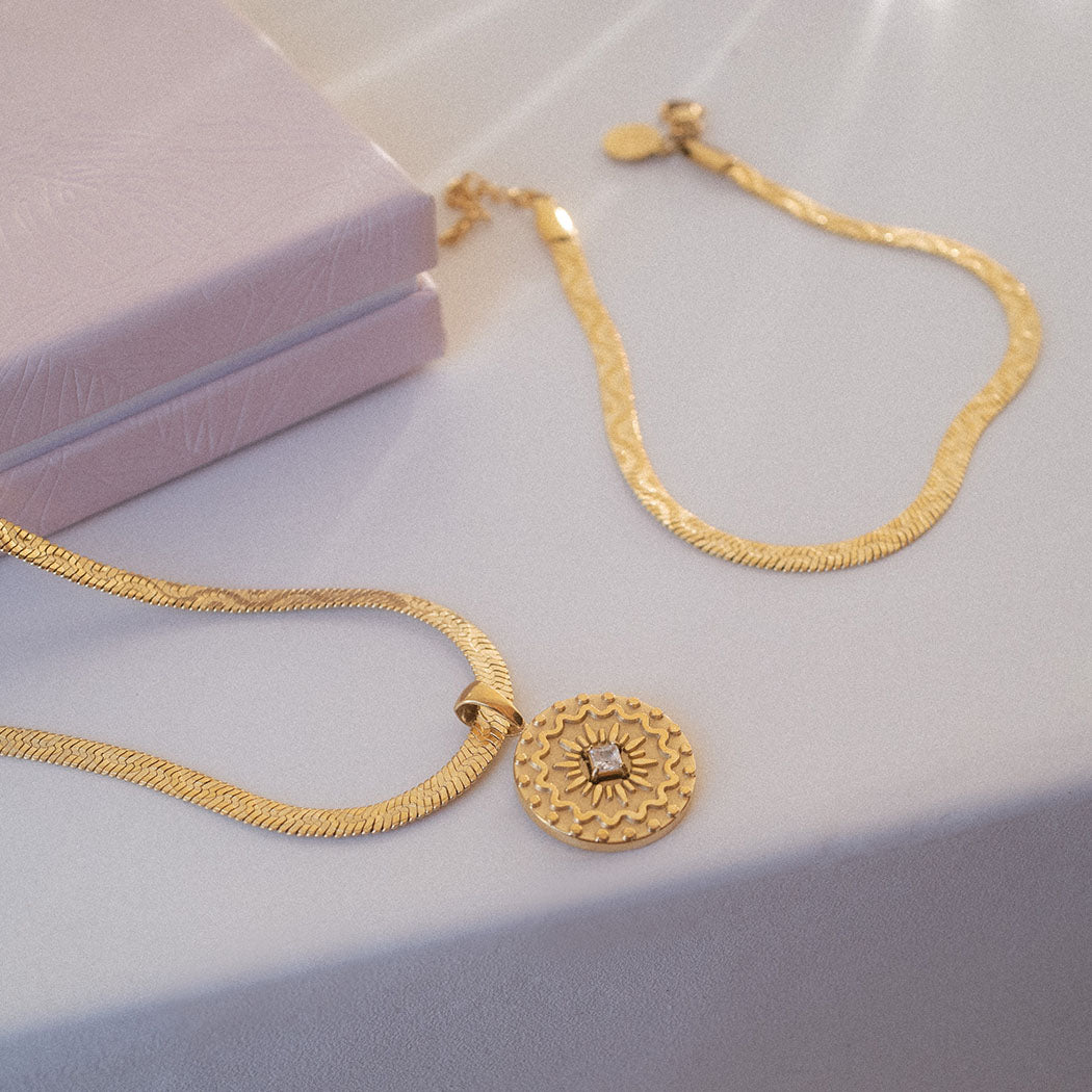 Goldene Kette mit Sonnenmotiv und Wellenstruktur von PURELEI, elegant auf hellem Stoff präsentiert.