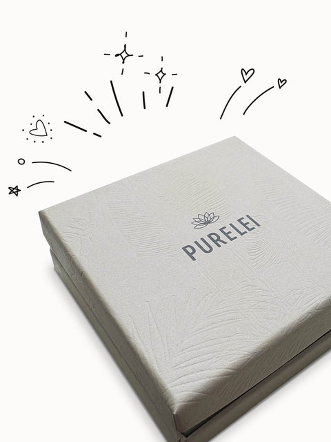 Elegante PURELEI Mystery Gift Box in cremeweiß mit Prägung und tropischem Design für eine stilvolle Überraschung.