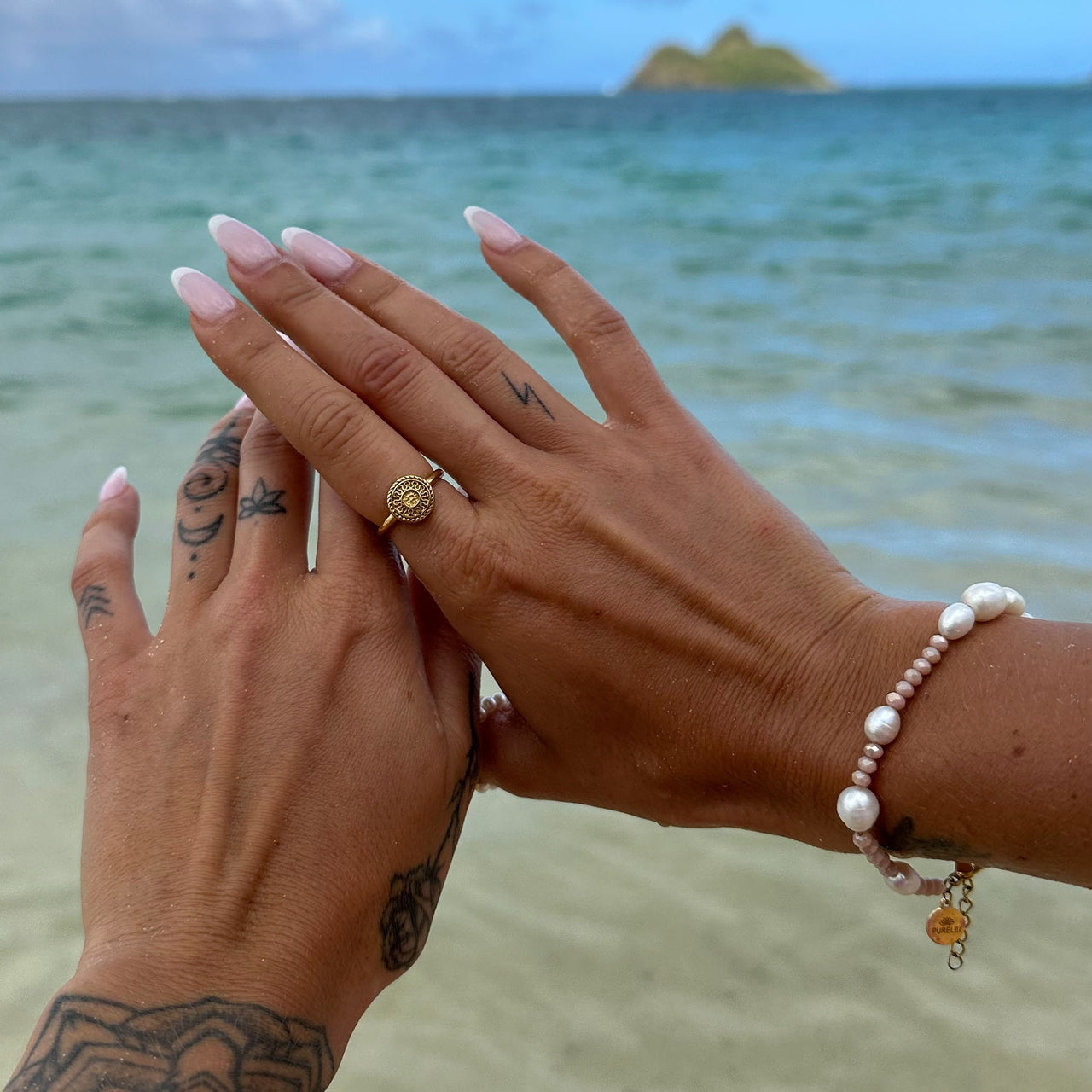 Waina Ring von PURELEI in Gold mit filigraner Prägung, getragen am Strand – elegant und zeitlos femininer Schmuck.