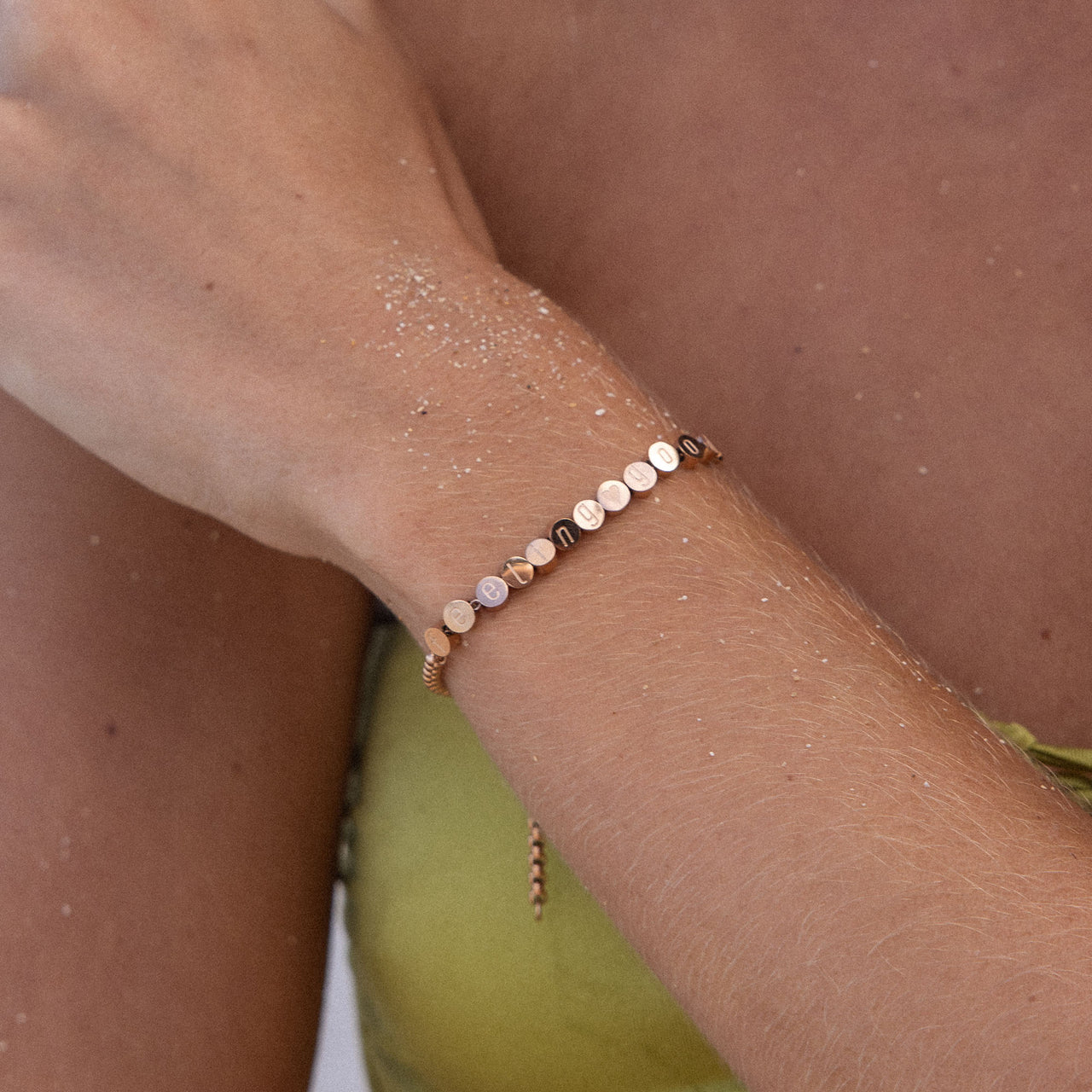 Feel Good Armband von PURELEI, vergoldet, fein mit positiven Botschaften, getragen am sonnenverwöhnten Handgelenk.