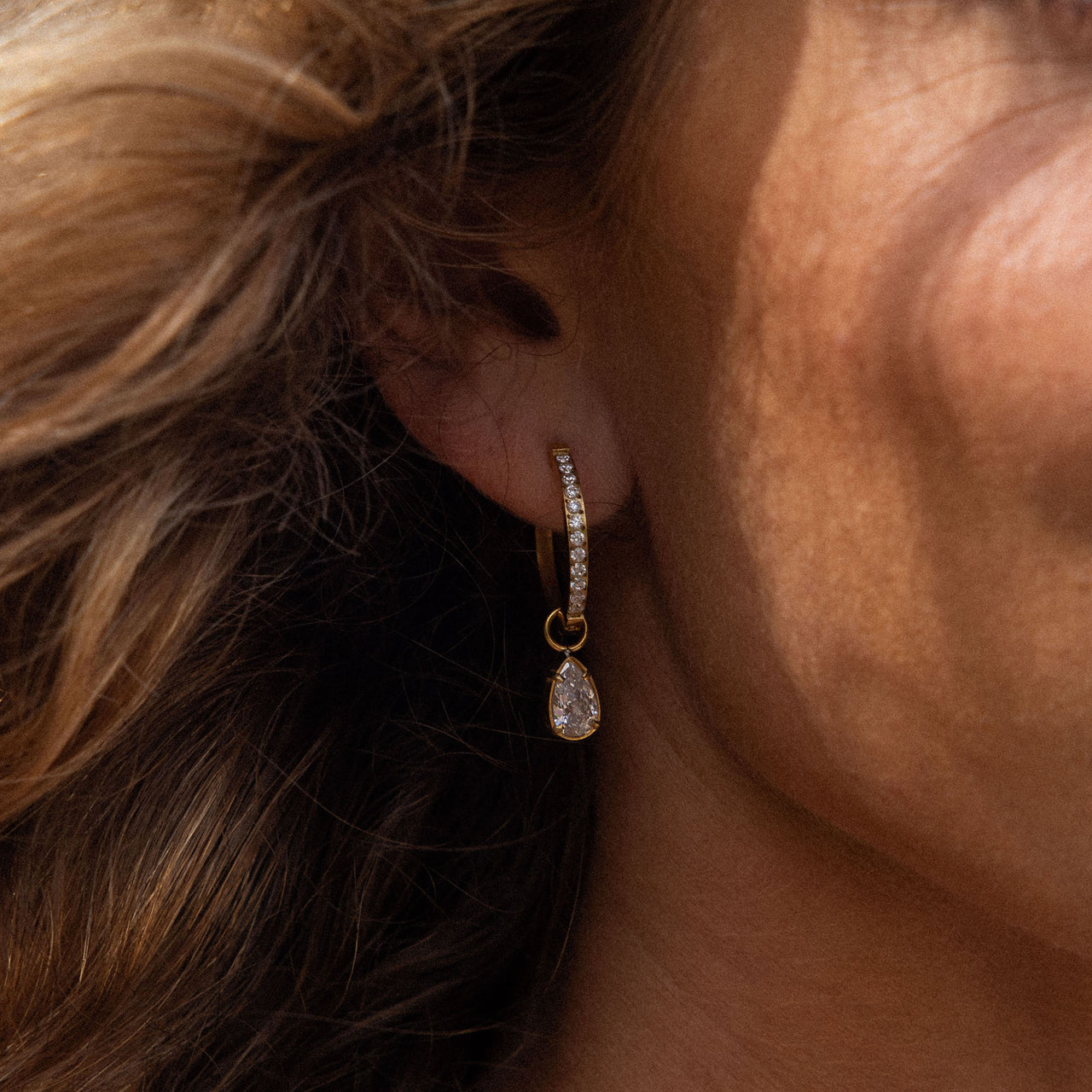 PURELEI Felice Ohrringe, goldene Creolen mit weißen Zirkonia-Tropfen, elegant getragen in warmem Licht