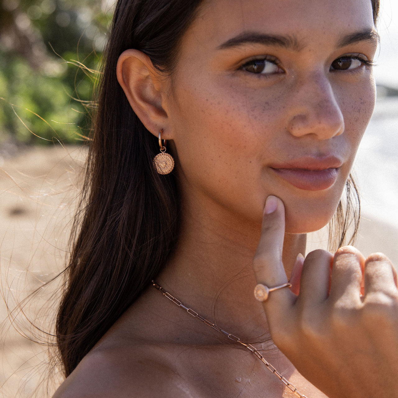 PURELEI Waina Ohrringe in Roségold mit filigranem Charm, getragen am sonnigen Strand – elegant und zeitlos.