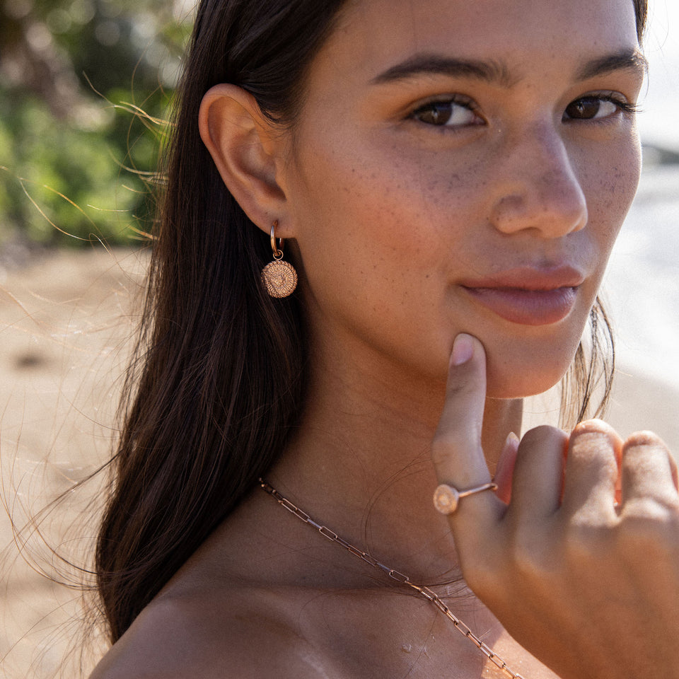 PURELEI Waina Ohrringe in Roségold mit filigranem Charm, getragen am sonnigen Strand – elegant und zeitlos.