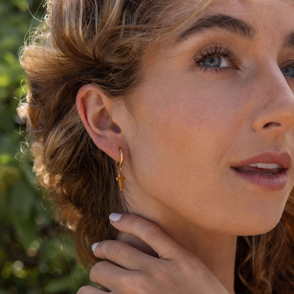 PURELEI Cross Creole Ohrringe aus 18K Gold mit Kreuzanhänger, elegant und femininer Island-Spirit, getragen im Sonnenlicht.