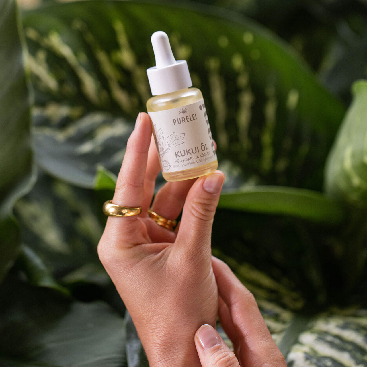 PURELEI Hawaiian Gloss Haircare Set Kukui Öl-Fläschchen in Hand vor tropischem Grün, elegant und natürlich.