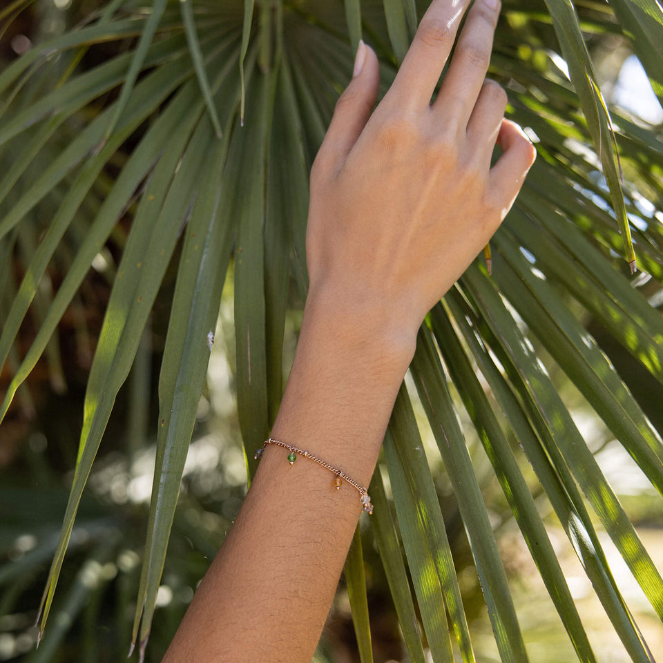 Boho Armband von PURELEI mit bunten Glasperlen, vergoldet, am Handgelenk vor grünem Blatt – sommerlich, feminin.