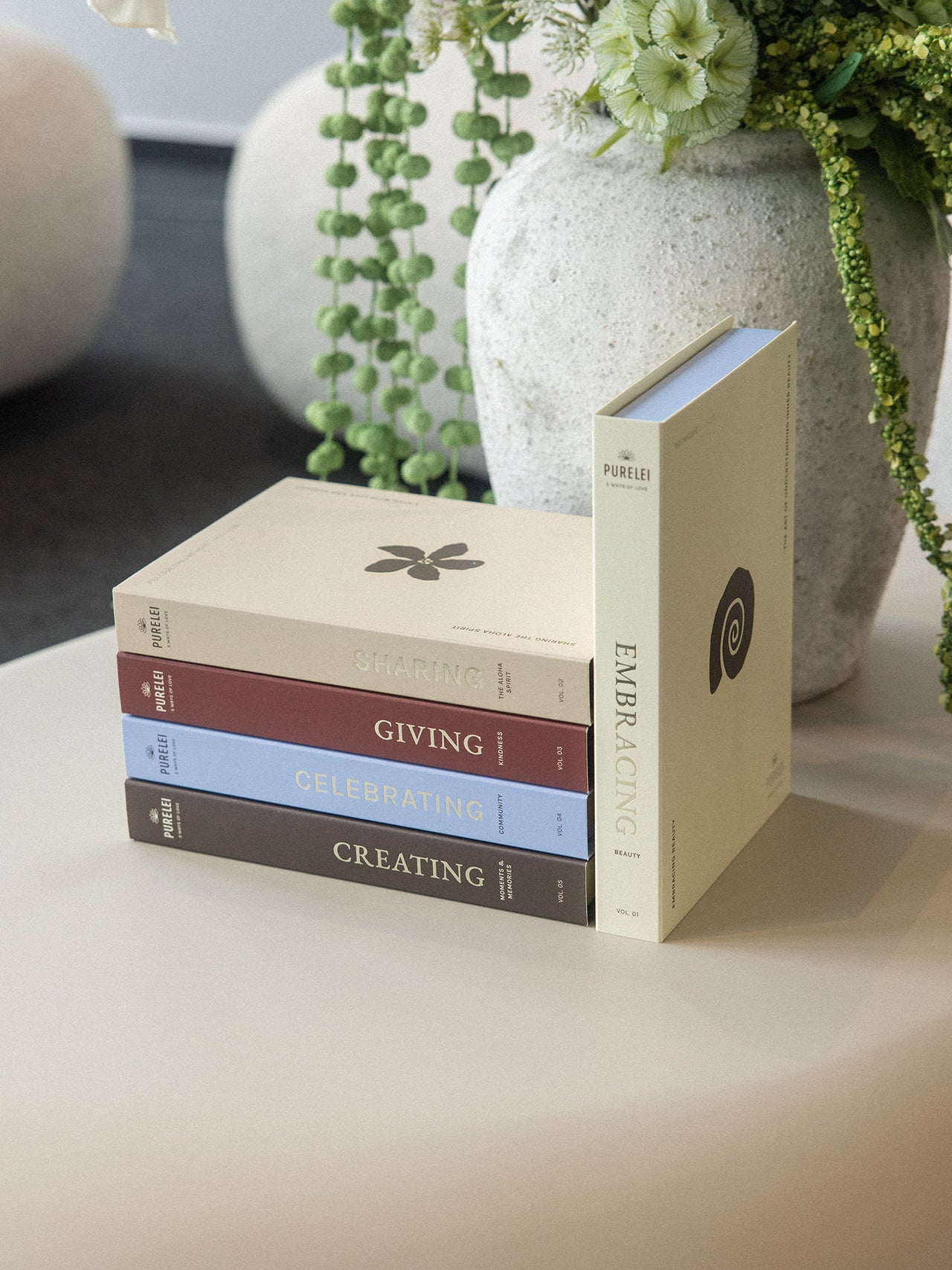 Bücher von PURELEI in sanften Farben auf einem Tisch, umgeben von Pflanzen.