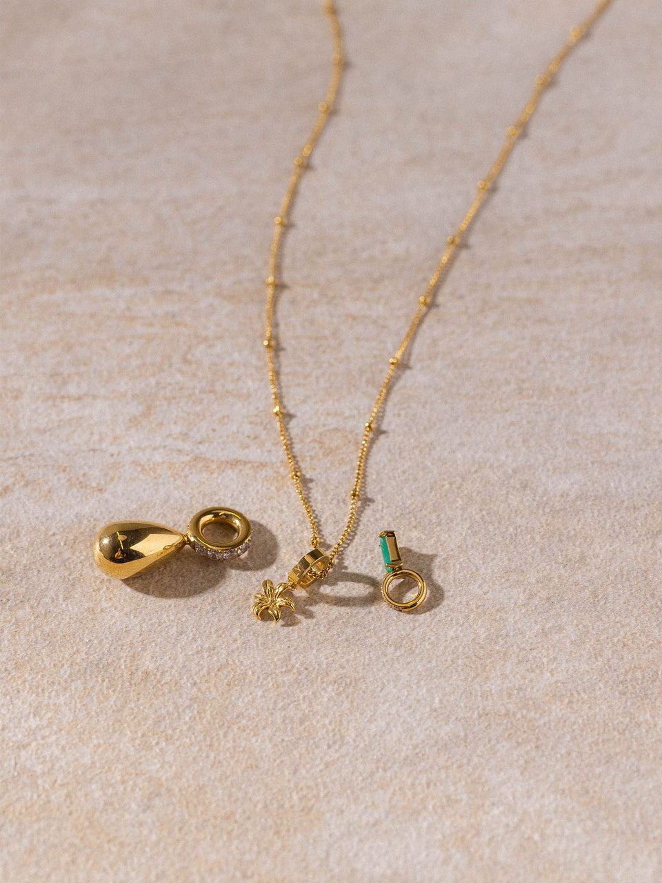 Feingliedrige Li’ili’i Kette in 18K Gold mit zarten Anhängern auf hellem Sand, PURELEI Style, elegant und feminin.