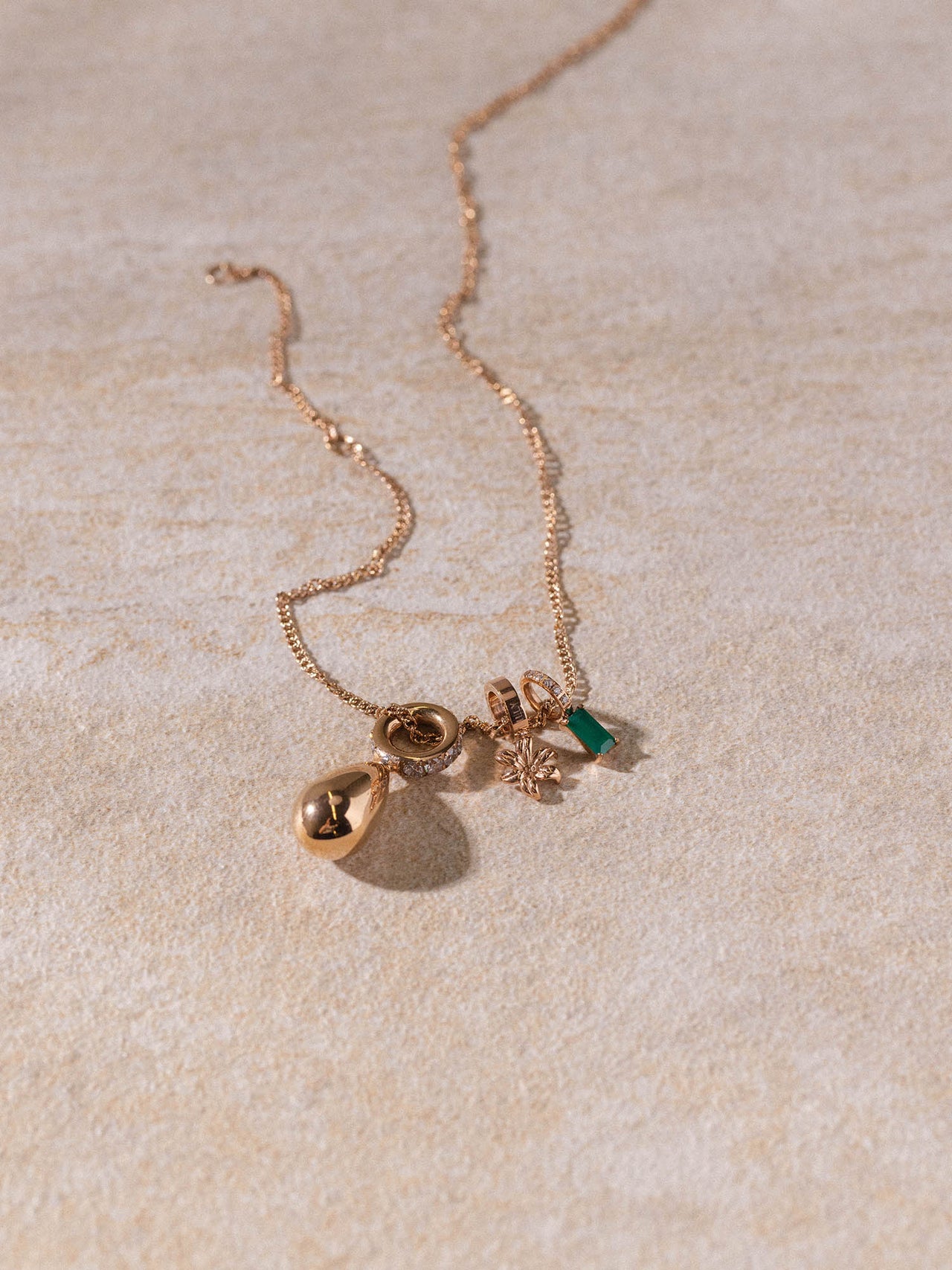 Kaula Kette von PURELEI in Roségold mit feinem, gedrehtem Design und zarten Anhängern auf hellem Sandstein.