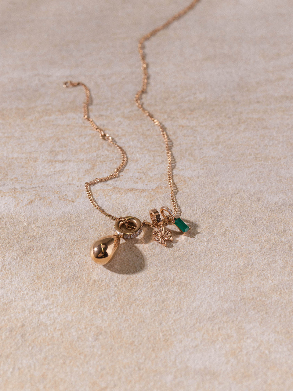 Kaula Kette von PURELEI in Roségold mit feinem, gedrehtem Design und zarten Anhängern auf hellem Sandstein.