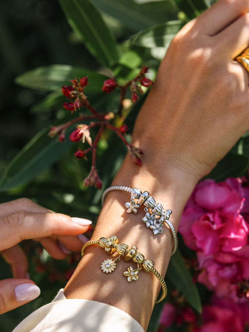 Zartes Lei Blume Stopper Charm in Gold und Silber, floral, nickelfrei, am Arm getragen vor tropischem Blütenhintergrund, PURELEI