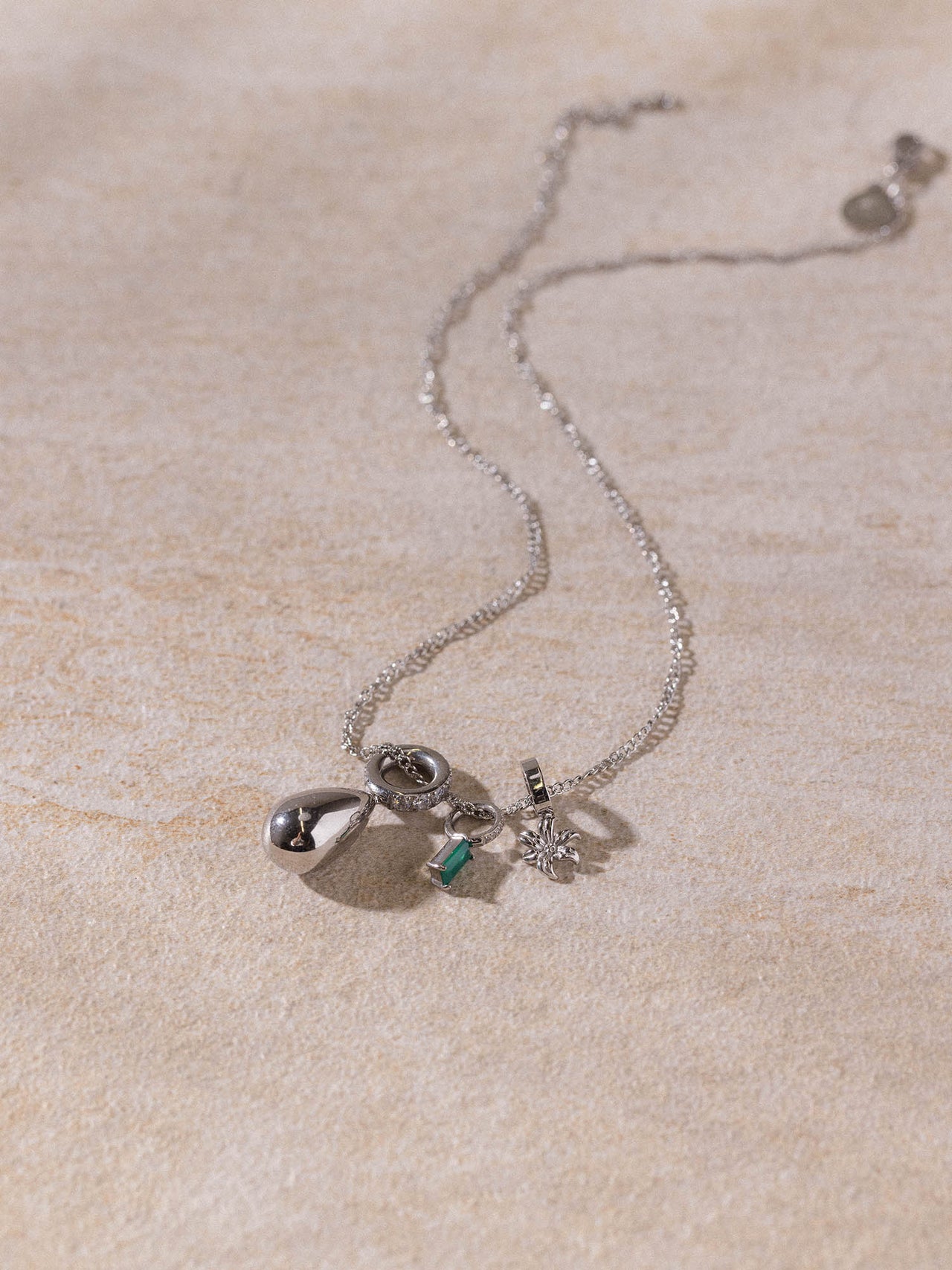 PURELEI Kaula Kette aus silberfarbenem Edelstahl mit feinen Anhängern auf hellem Sandstein, elegant und feminin.