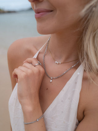 Zarte PURELEI Kette mit Perlen und Silberarmband, getragen am Strand, strahlt Eleganz aus.