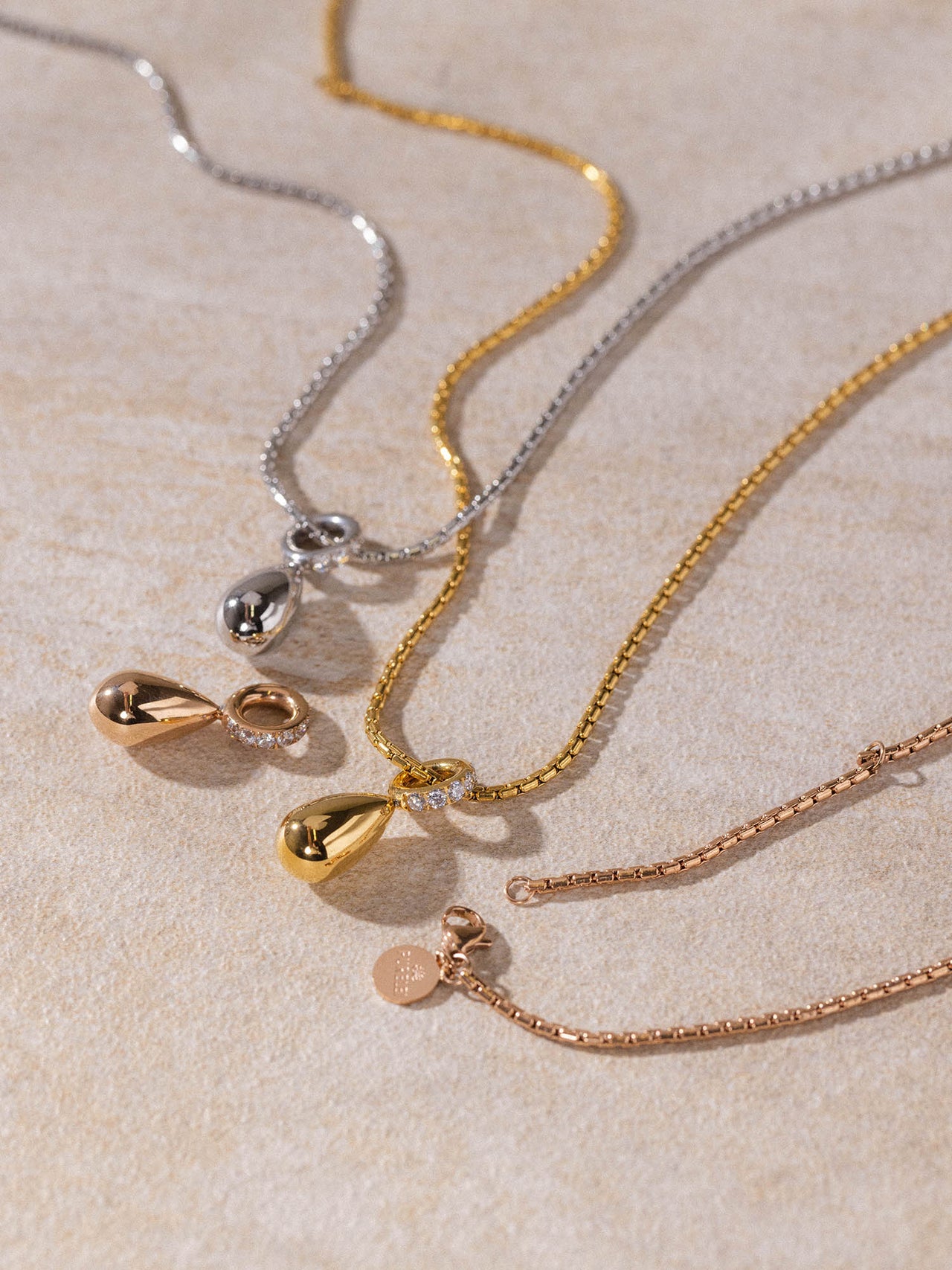 Resonance Kette von PURELEI in Gold, Silber und Roségold mit Tropfen-Anhängern, elegant auf hellem Untergrund präsentiert.