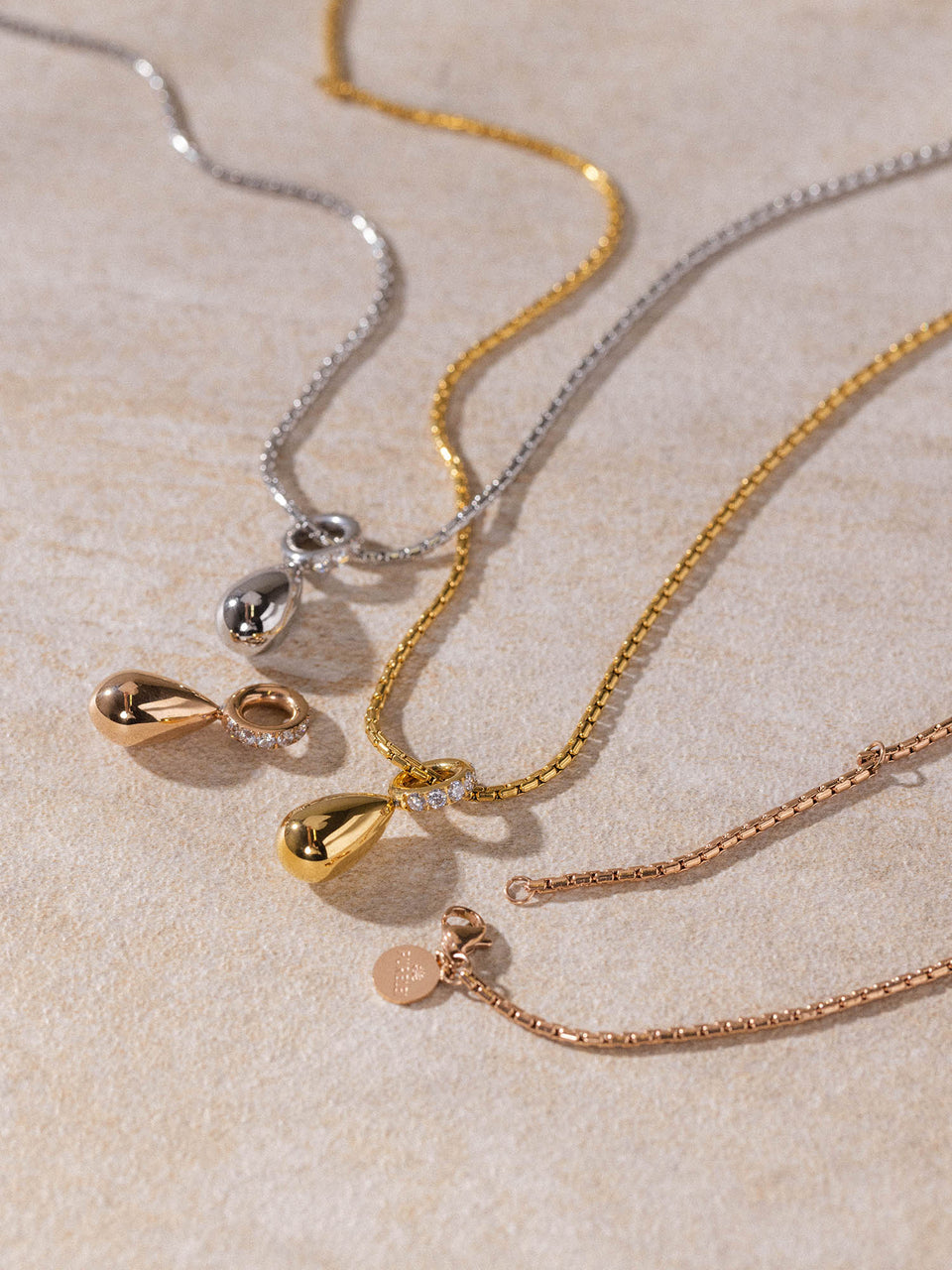 Resonance Kette von PURELEI in Gold, Silber und Roségold mit Tropfen-Anhängern, elegant auf hellem Untergrund präsentiert.