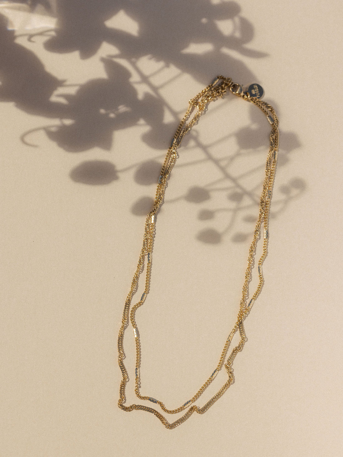 Mehrsträngige Kette aus goldfarbenem Material, elegant drapiert mit Schattenwurf, PURELEI.