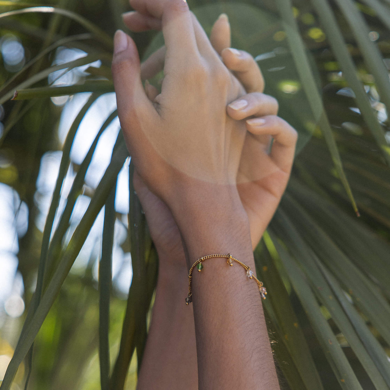 PURELEI Boho Armband aus 18K Gold mit bunten Glasperlen, zart am Handgelenk vor tropischem Grün getragen.