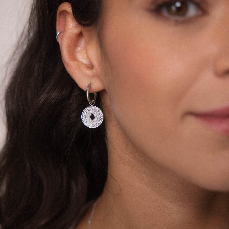 PURELEI Lolani Ohrringe aus silbernen Creolen mit gemustertem Coin, elegant und feminin am Ohr getragen.
