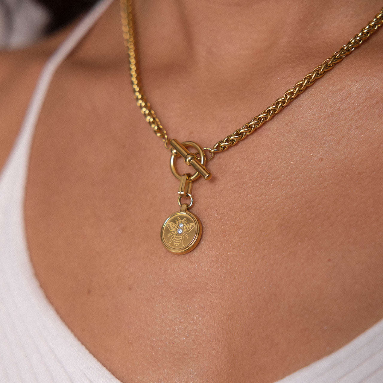 Goldene PURELEI Lele Kette mit filigraner Bienen-Gravur und Schmucksteinen, elegant am Hals getragen.