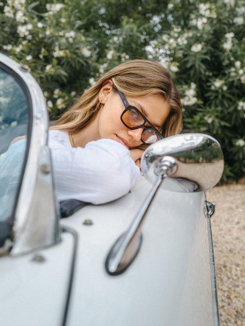 Summer Haze Sonnenbrille von PURELEI mit schwarzem Acetat und braunen Gläsern, elegant am Oldtimer gelehnt.