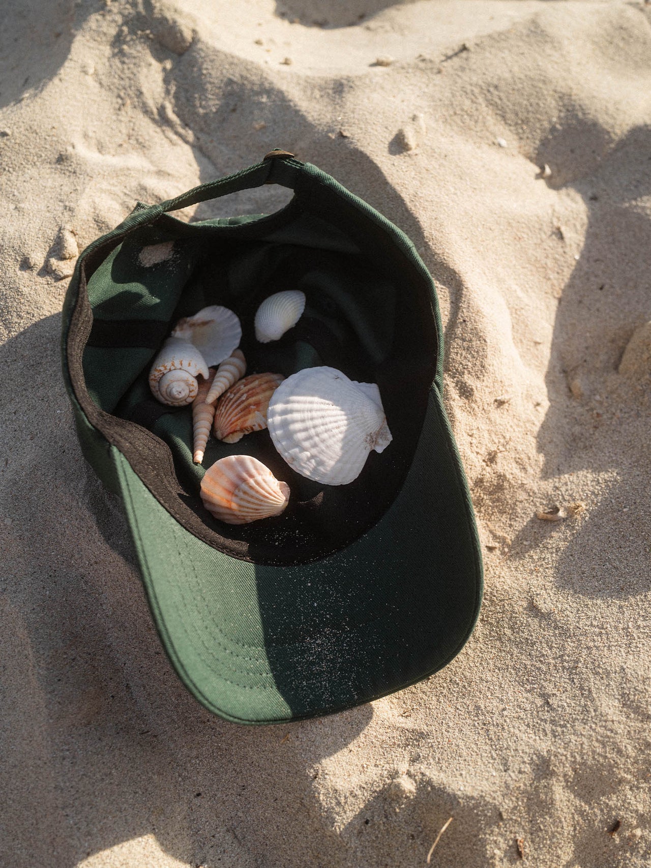 Island Kappe von PURELEI in Grün/Weiß aus Baumwolle, liegt im Sand mit Muscheln – natürlicher Island-Spirit.