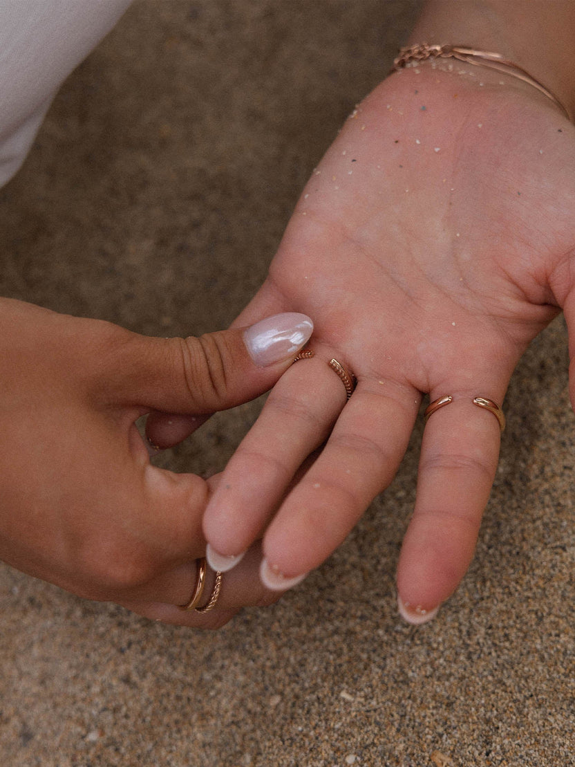 Roségoldene Ringe auf einer Hand, umgeben von Sand, PURELEI inspiriert.