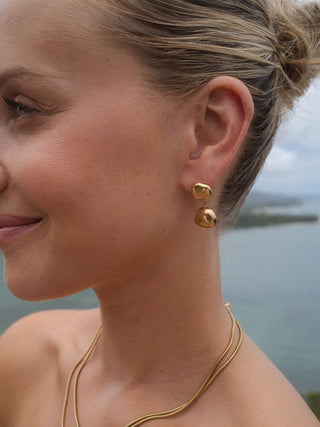 Roségoldene Ohrringe mit geschwungenem Design, getragen in maritimer Umgebung – PURELEI.