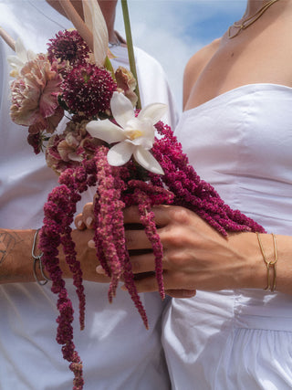 Zartes Armband von PURELEI, roségold, getragen mit bunten Blumen im Hintergrund.