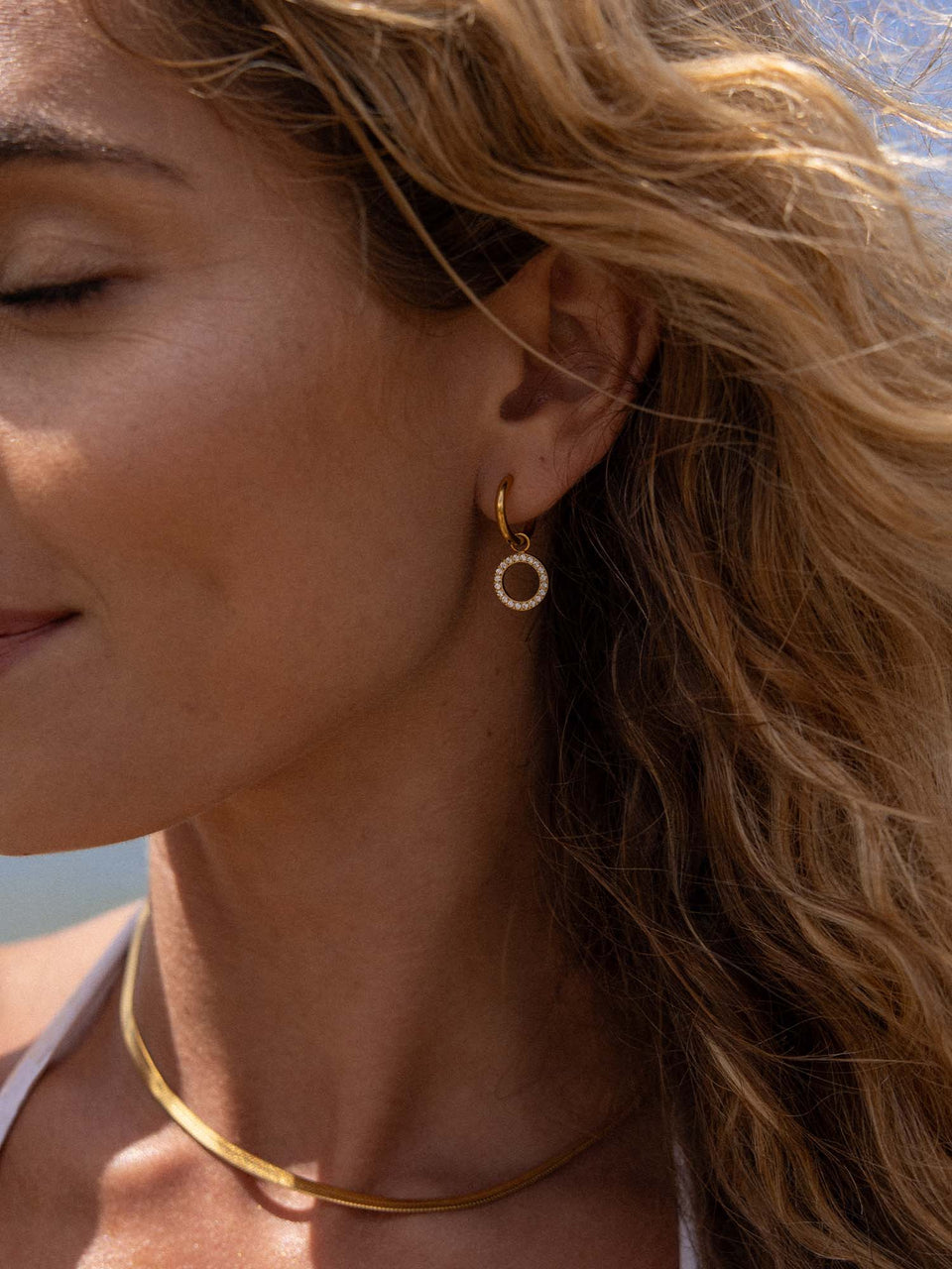 PURELEI Closed Glow Ohrringe Gold mit funkelnden Zirkonia, eleganter Glow-Look, sonnenverwöhnte Haut am Strand