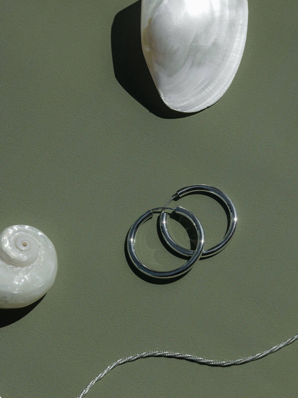 PURELEI Timeless Ohrringe aus glänzendem Silber, minimalistisch, elegant inszeniert mit Muscheln für Insel-Feeling.