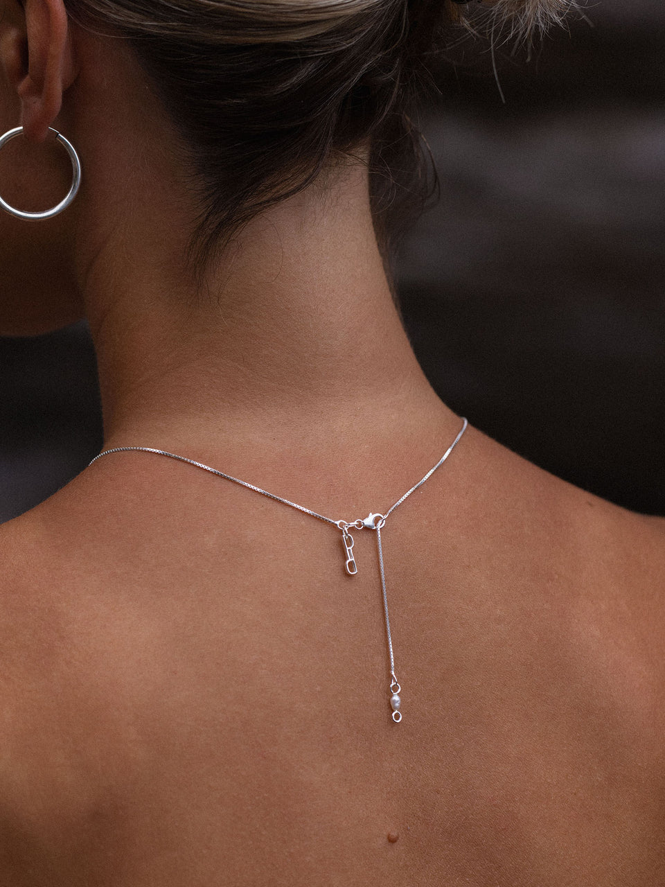 Perfection Kette aus recyceltem Silber mit feiner Venezianerkette und PURELEI-Logo an nacktem Rücken getragen.