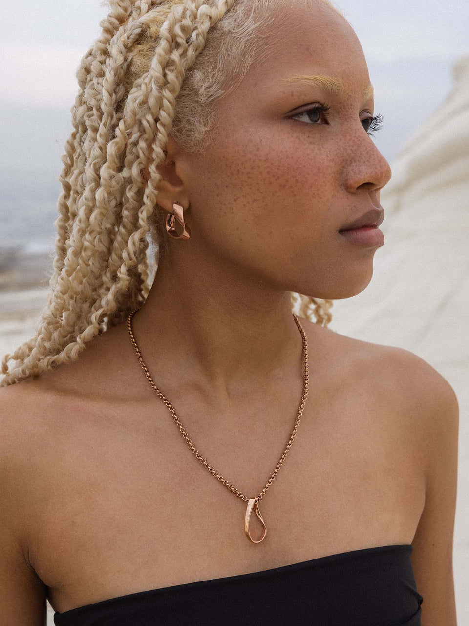 PURELEI River Ohrringe in Roségold mit geschwungener Form, getragen am Strand – elegant und feminin.