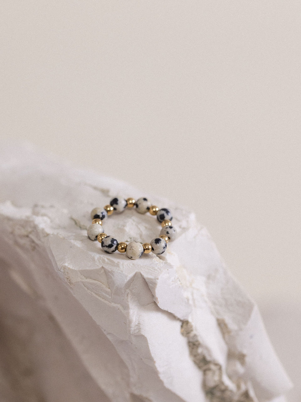 PURELEI Anxiety Coast Ring mit Dalmatiner-Jaspis und goldenen Edelstahlperlen, elegant auf hellem Stein inszeniert.